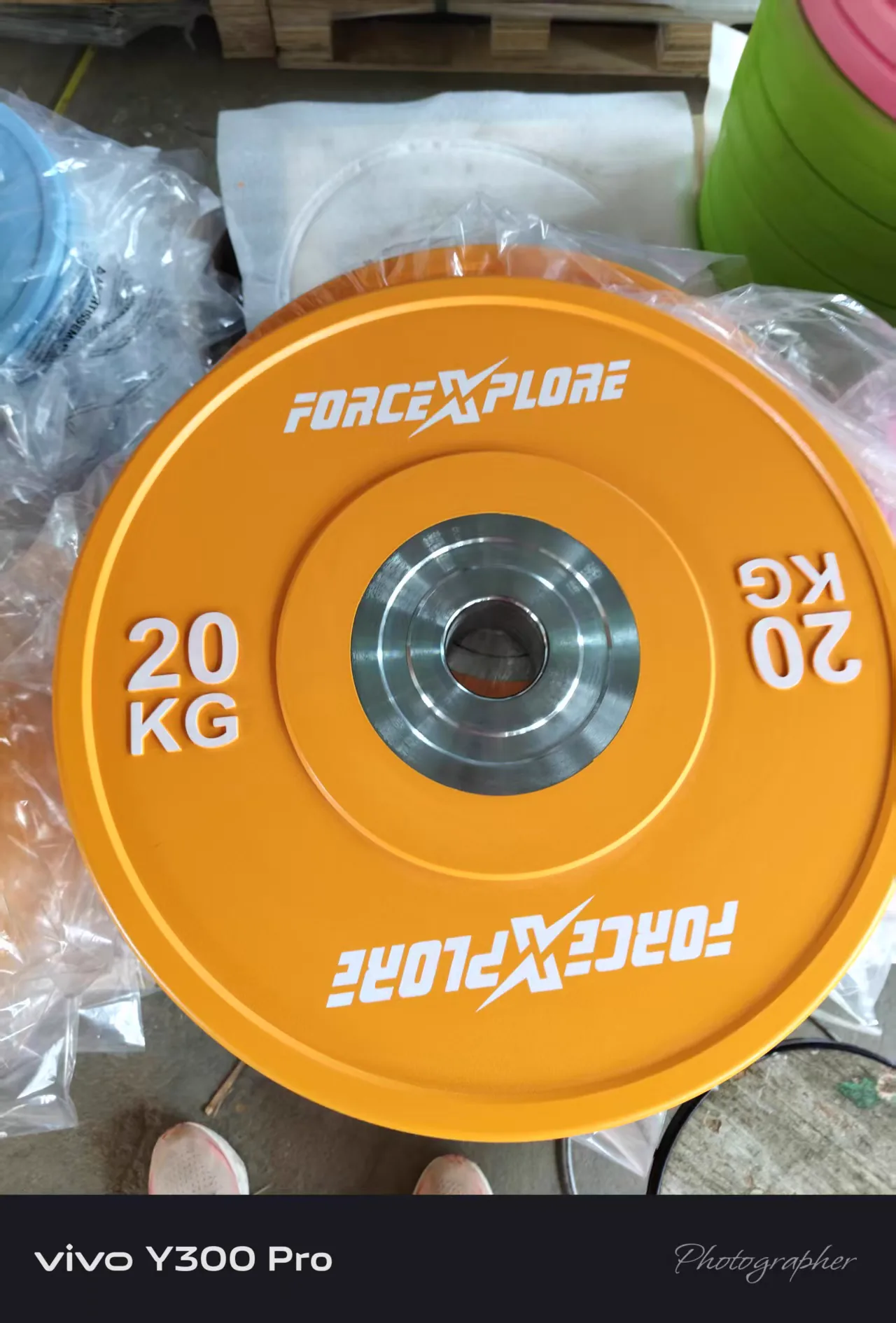 Orange 20 kg custom barbell plate prepared for a fitness chain strength area
