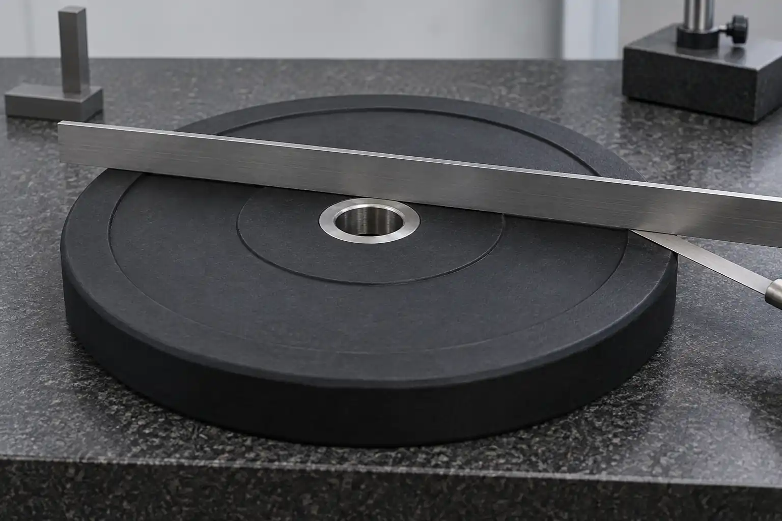 Unbranded Olympic weight plate on a granite reference with a straightedge for a flatness check